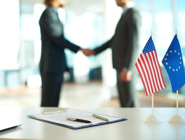 American flag, flag of European Union and business contract on background of two political leaders handshaking